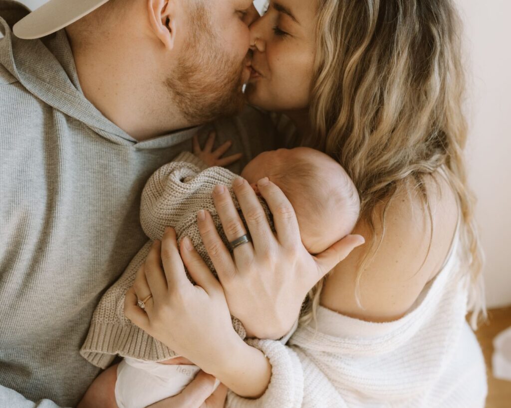 Mom and dad kiss while holding newborn baby