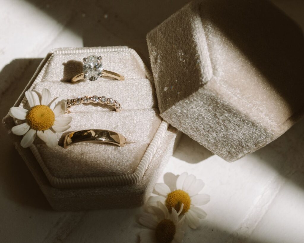 Bride and Groom's rings placed in a nude velvet box and laid in a stripe of afternoon light. Surrounded by little white flowers left over from the bride's bouquet. 