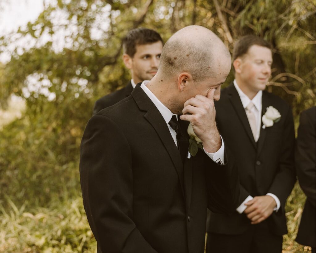 The groom wiping a tear from his eye as his bride makes her way down the aisle.