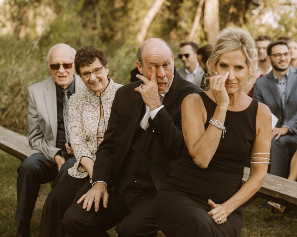 The grooms parents wiping tears from their eyes as they watch their son tear up as his bride comes down the aisle. 