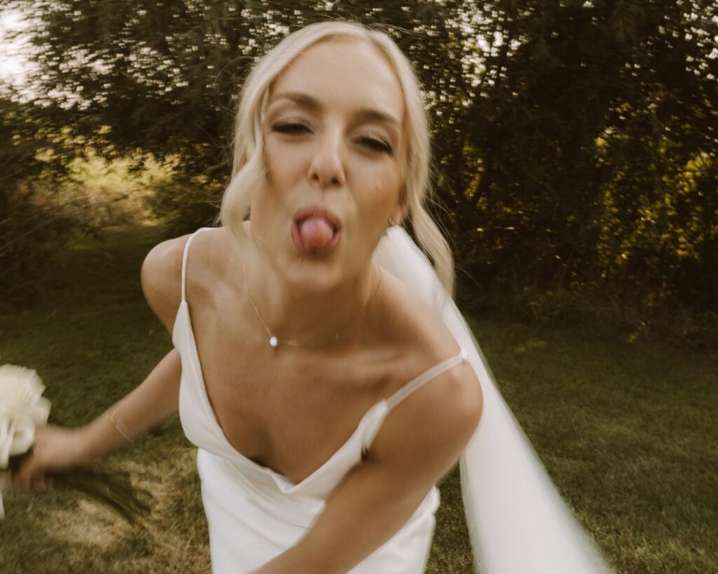 The bride leaning in towards the camera and sticking her tongue out.