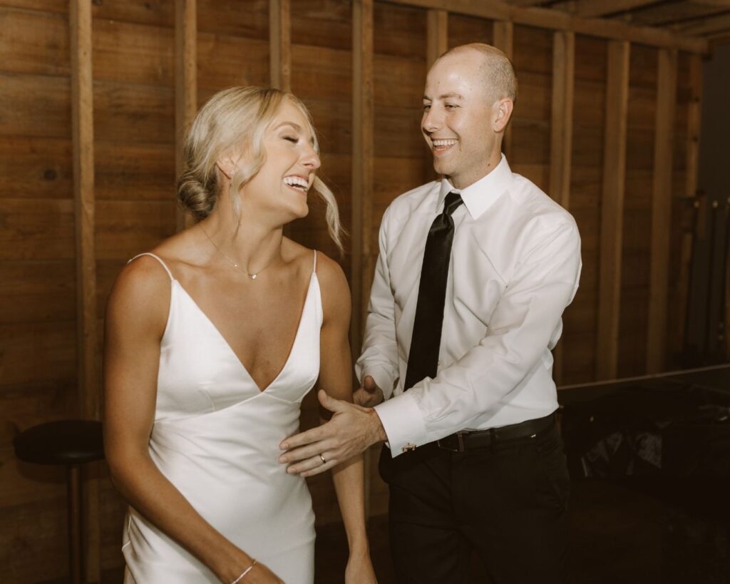 The bride and groom giggling at each other in the groom's suite as they practice their choreographed grand entrance dance.