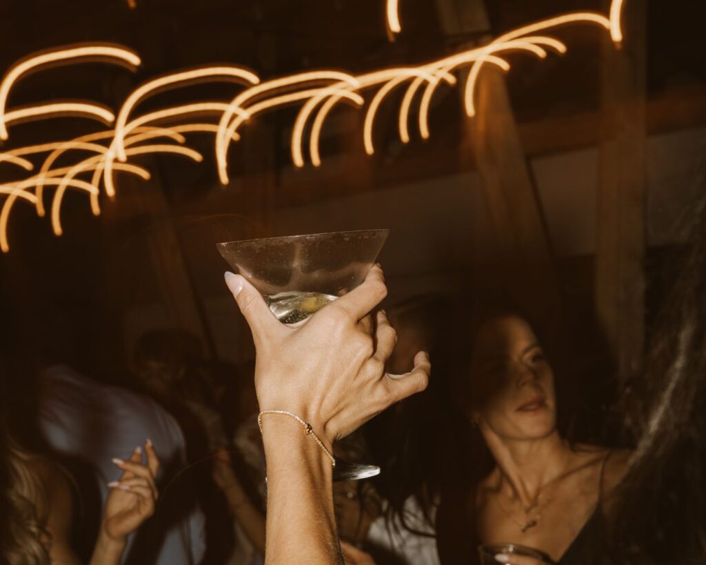 A flash photo of the brides hand holding her martini glass in the air while she dances with her guests.