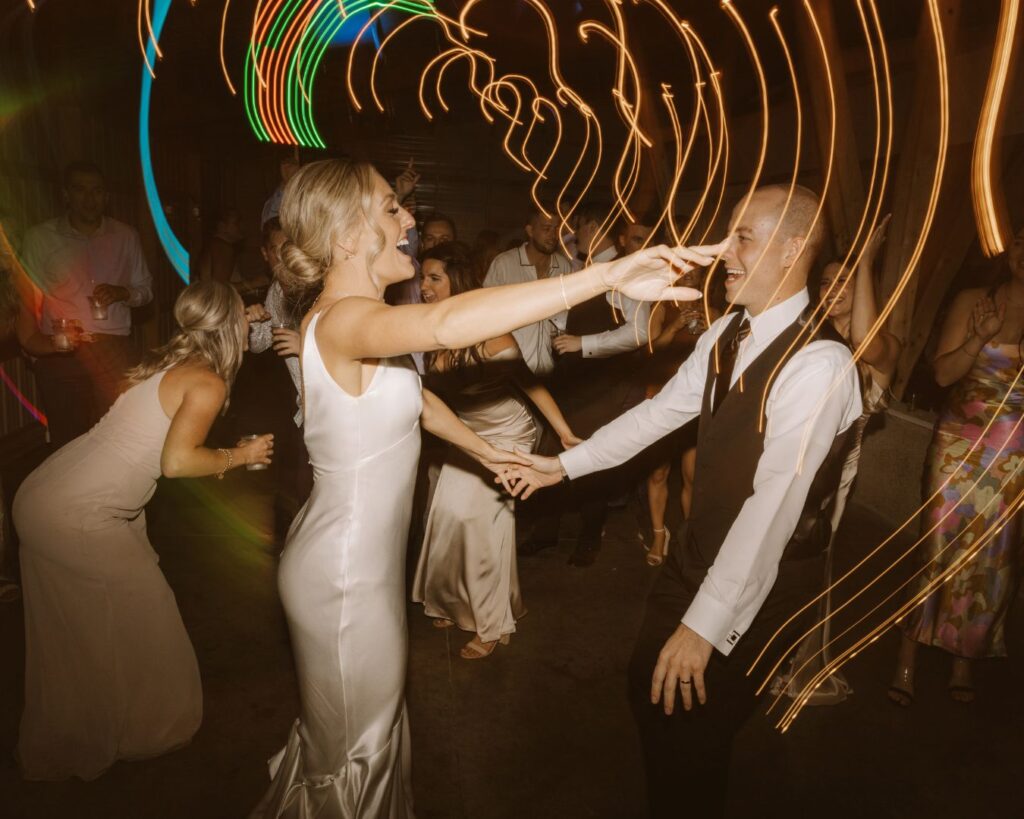 A flash photo of the bride and groom dancing together amongst their guests with the lights dragging around them.