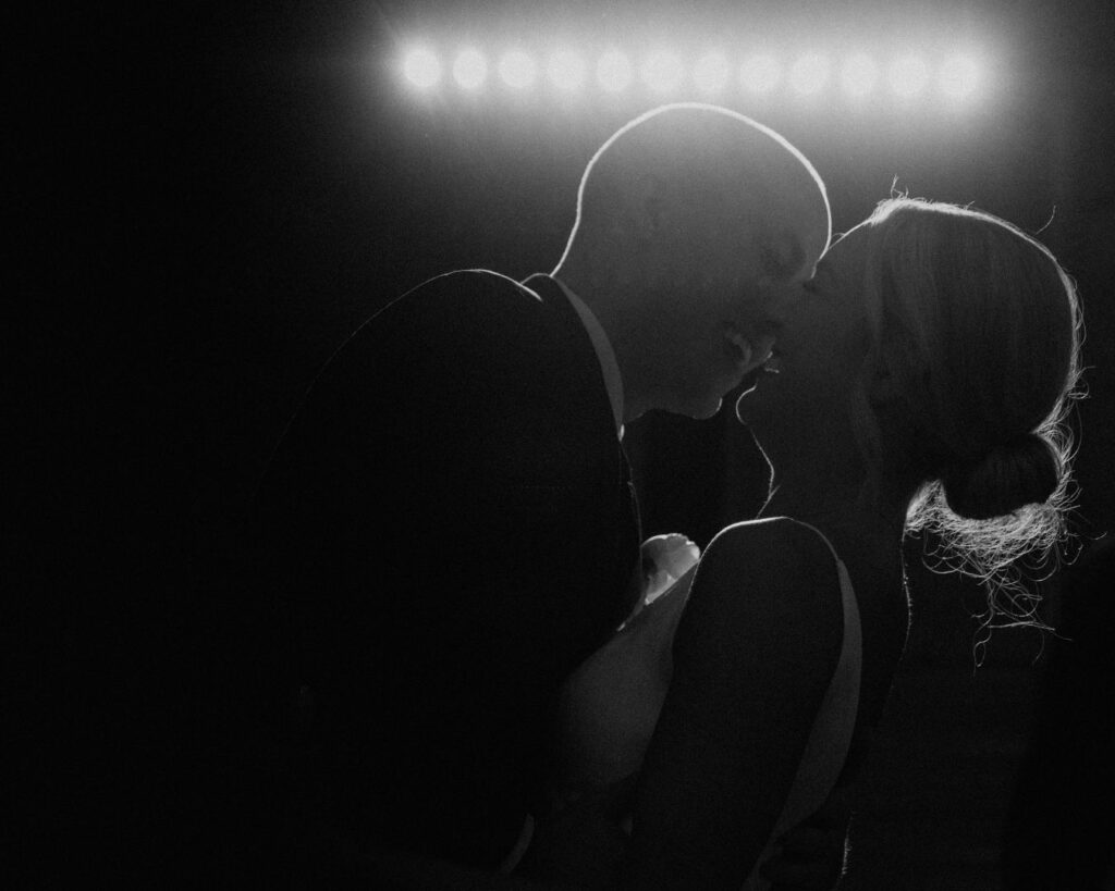 A black and white image of the bride and groom silhouetted by the DJ's lights, smiling just before a kiss.