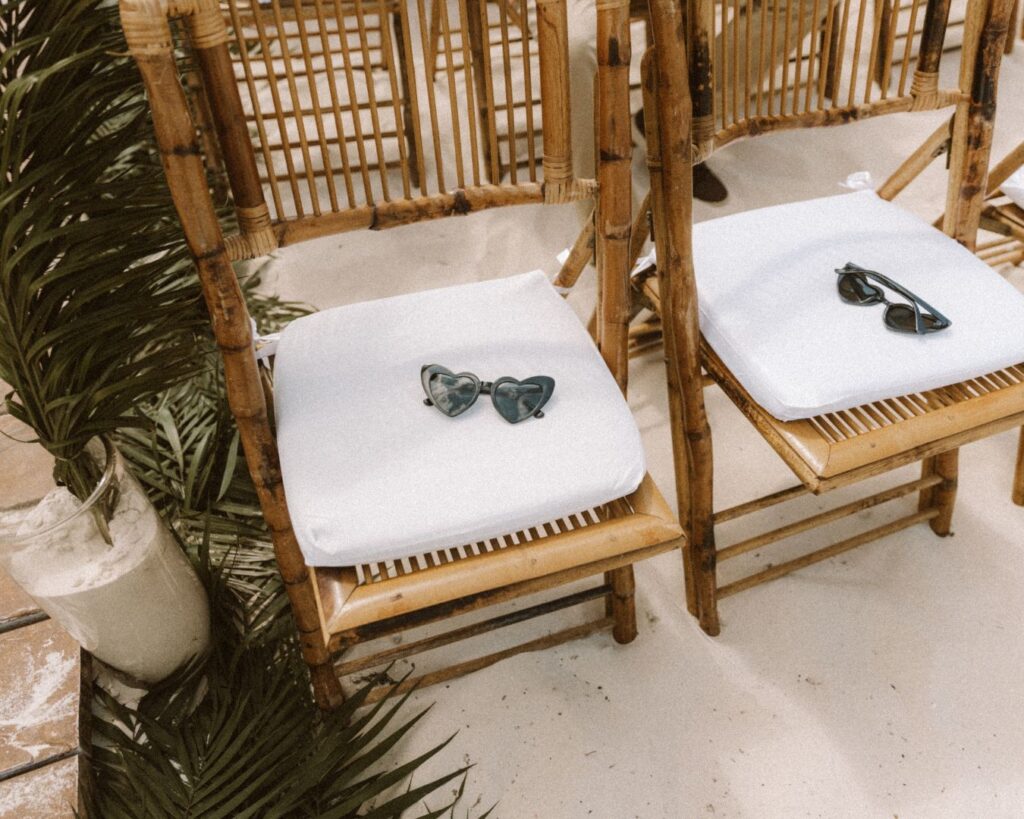 Heart shaped sunglasses laid on one of the bamboo chairs at the ceremony on the beach. 