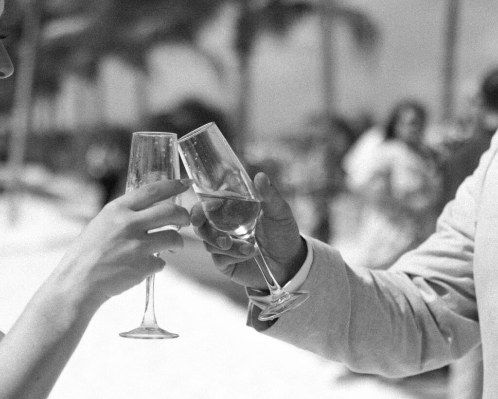 A grainy black and white image of the bride and groom's hands cheers-ing their glasses of champagne after the ceremony. 