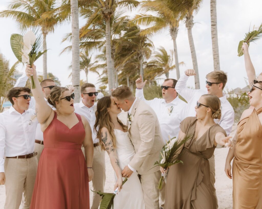 The bride and groom kissing while the bridal party surrounds them cheering. 