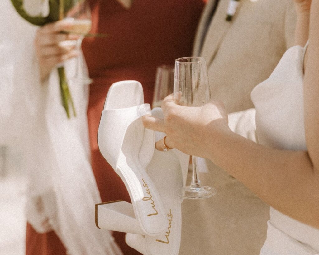 up close image of the bride's ring hand holding her shoes and a glass of champange