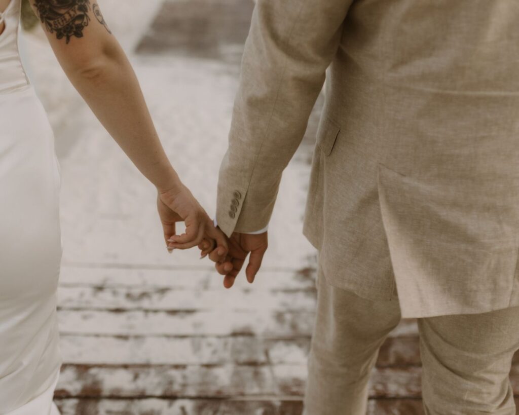 Image of the bride and groom holding hands as they walk back to their party on the boardwalk.  