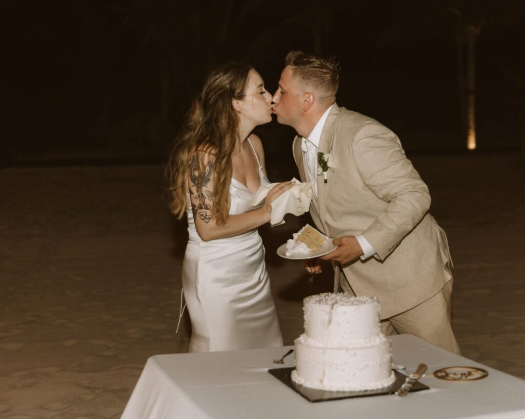 The bride and groom kissing on their wedding day right after cutting their white pearl covered cake. 