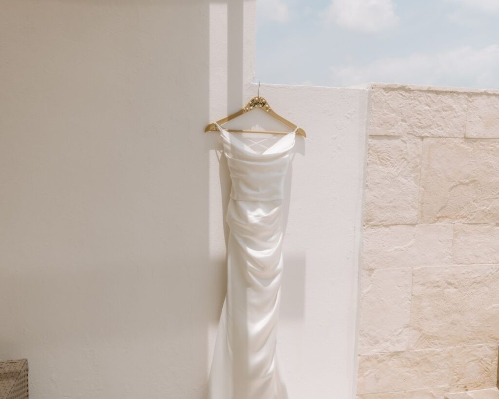 Bride's dress hung against a white wall with shadows laying over it from the sun. 