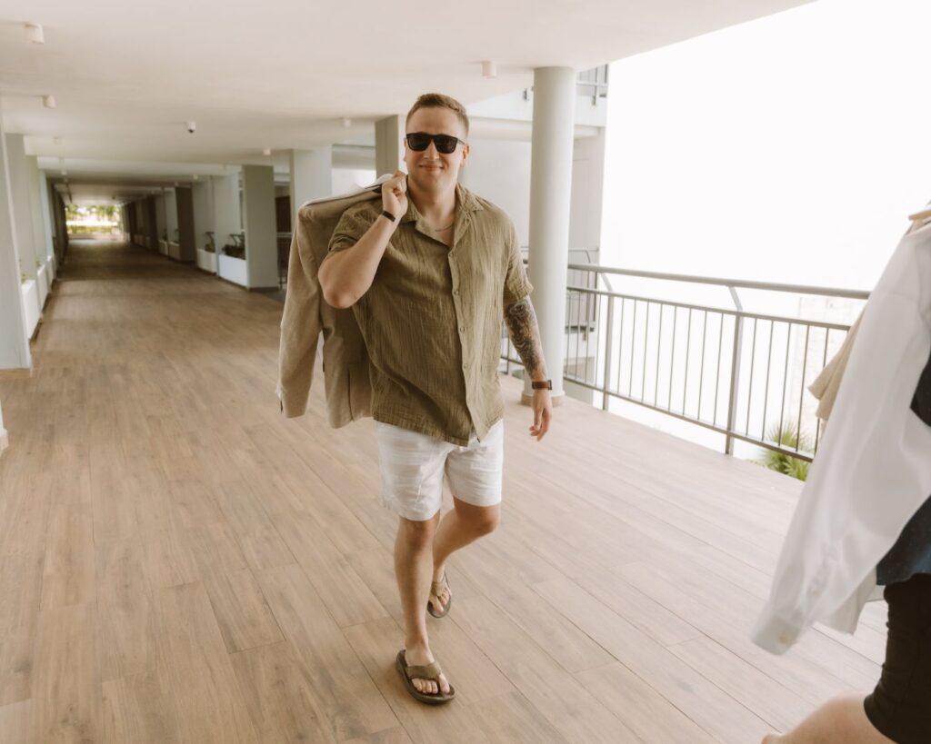 The groom walking to the space where he is getting ready with his suit slung over his shoulder. 