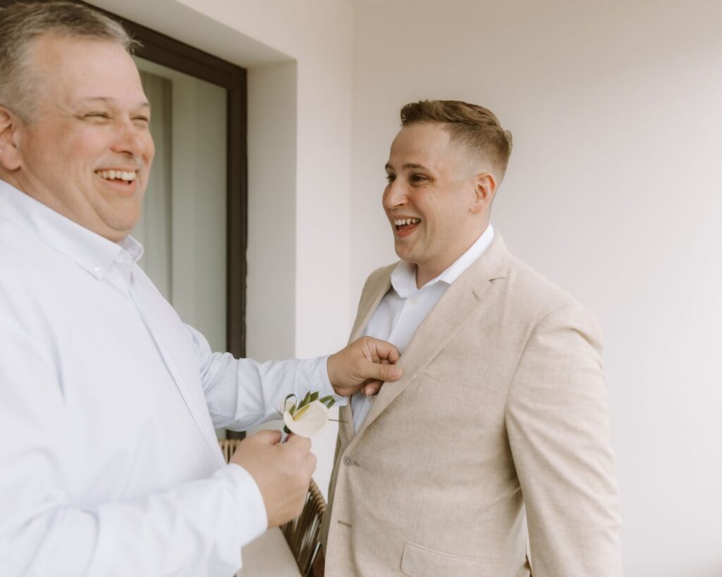 The groom laughing with his dad as his dad puts his boutonniere on.  