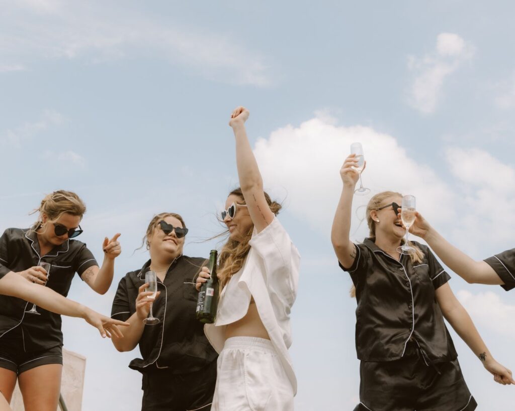 The bride and bridesmaids dancing in their getting ready pj's, champagne in hand and blue skies behind them. 