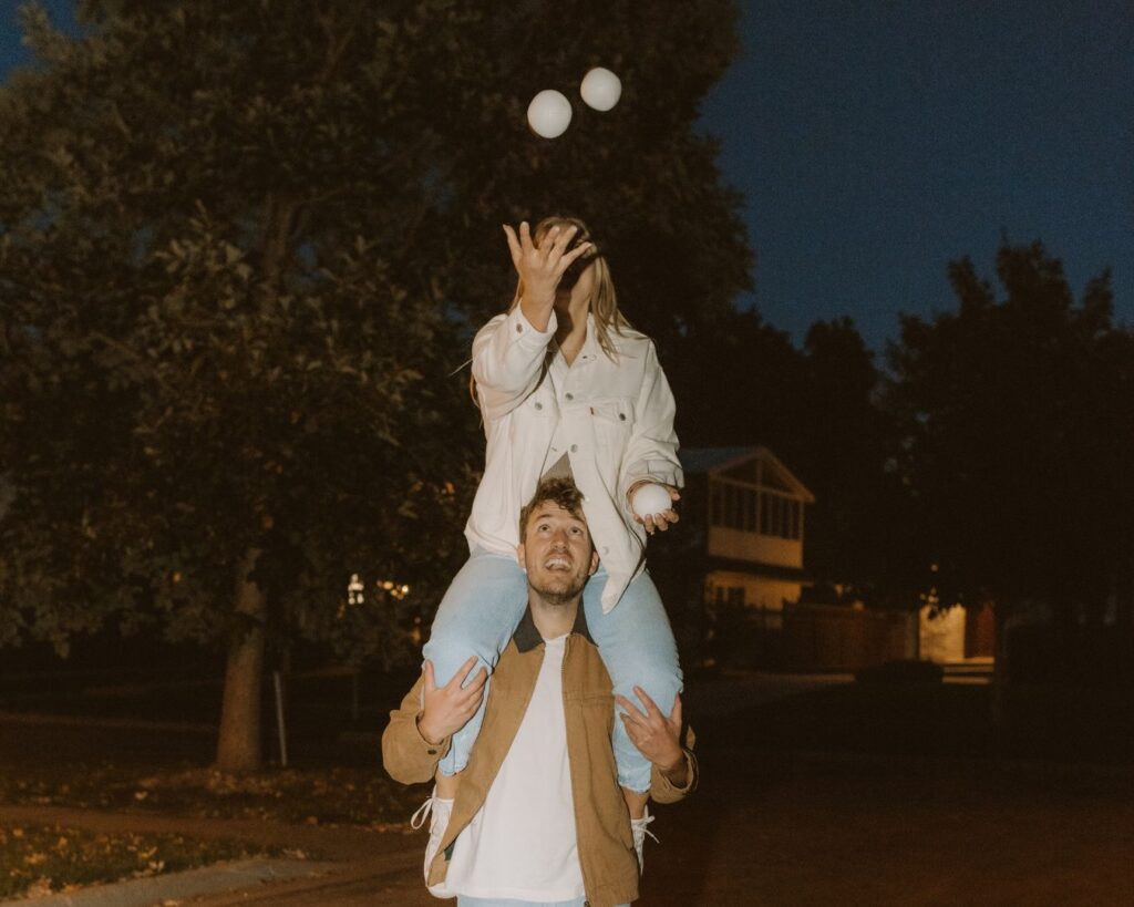 Engaged couple juggling in the street while she sits on his shoulders. 