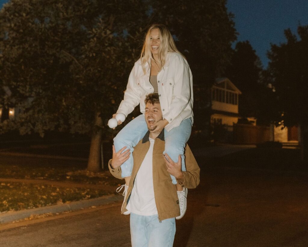 Couple laughing while she sits on his shoulders after dropping a ball during an attempt at juggling while also keeping balance. 