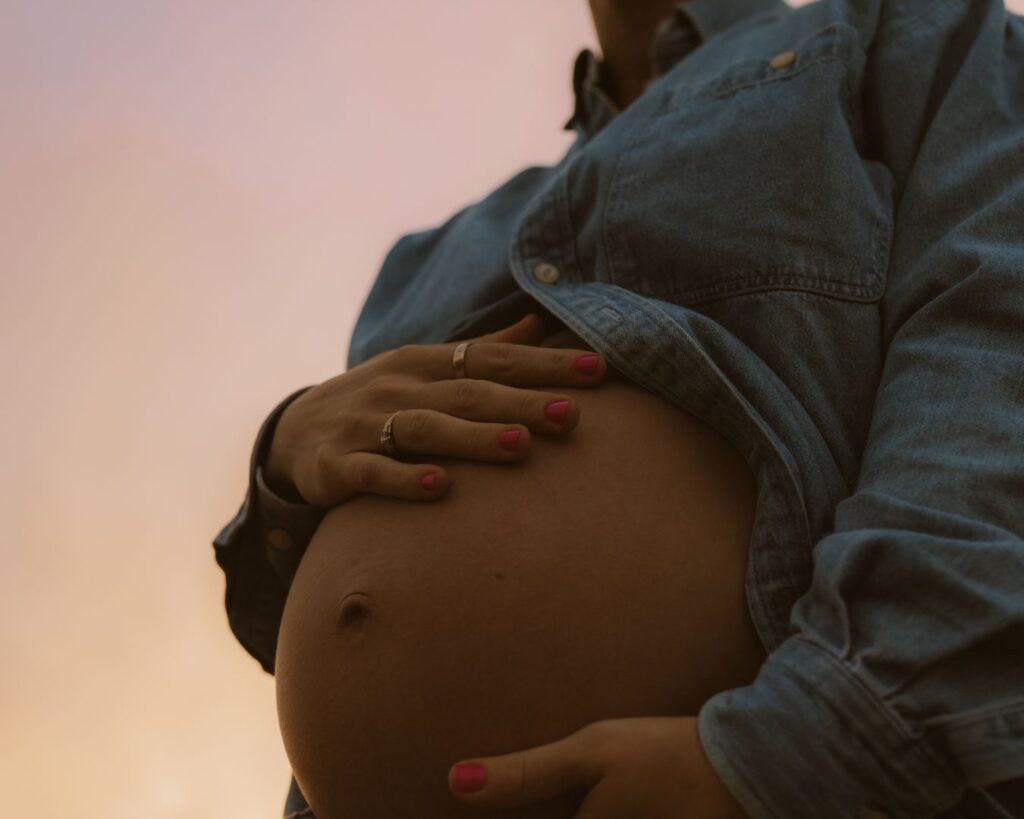 Pregnant mom caressing her belly as the pinks and oranges of the sunset behind her start to show off during her maternity session. 