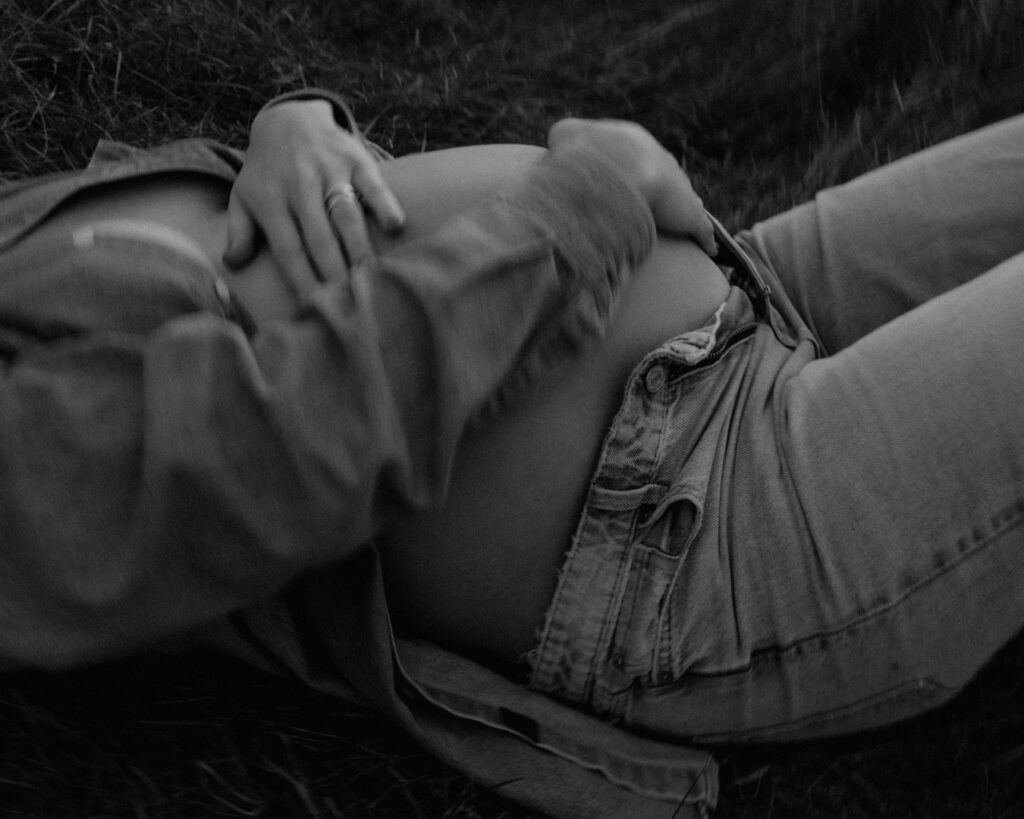 Black and white image of pregnant mom caressing her bare belly while laying in a field during blue hour. 