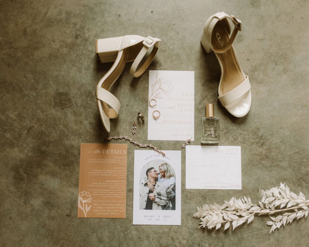 Brides details- shoes, rings, jewelry, perfume- scattered around the bride and grooms invite suite and save the date. 