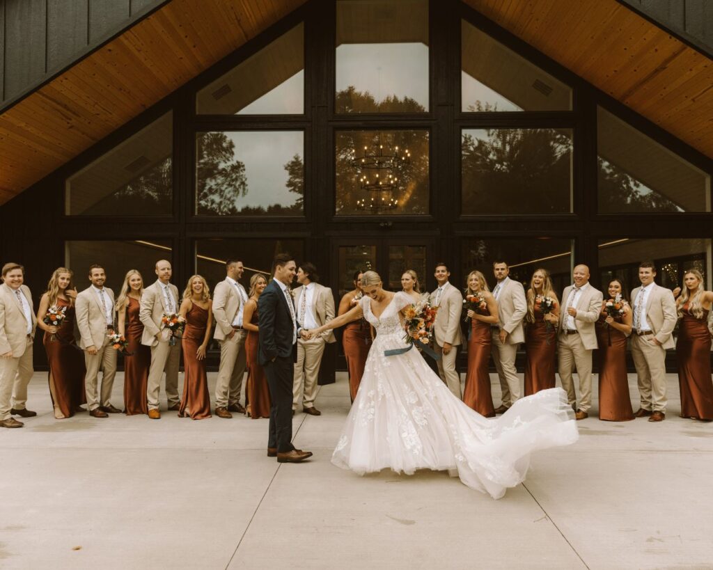 Groom spinning bride as their bridal party cheers them on from behind them.