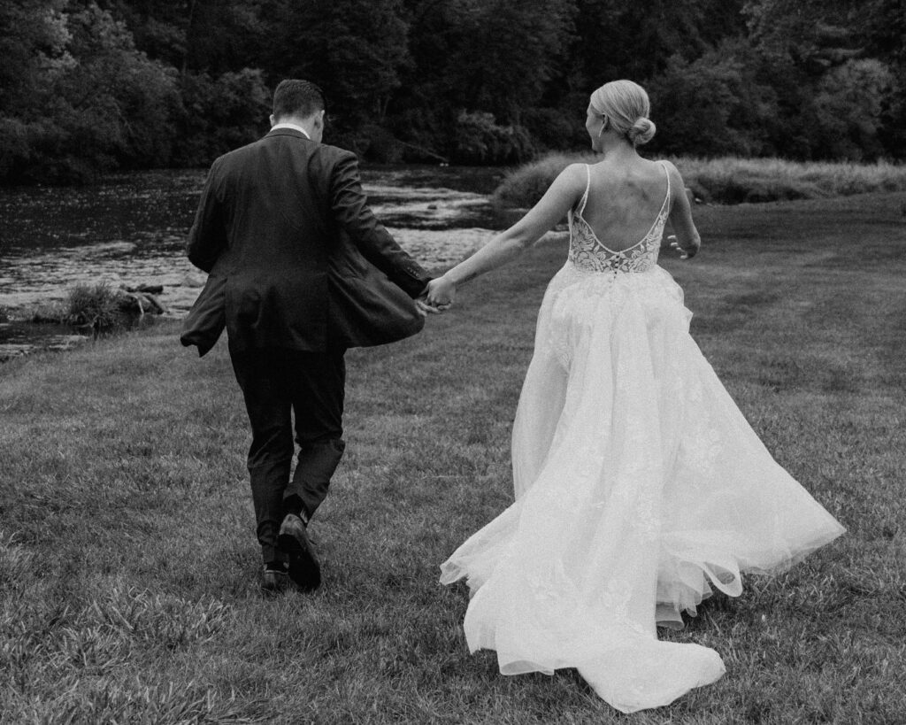 Black and white image of the bride and groom running away from the camera, her dress flowing behind her.