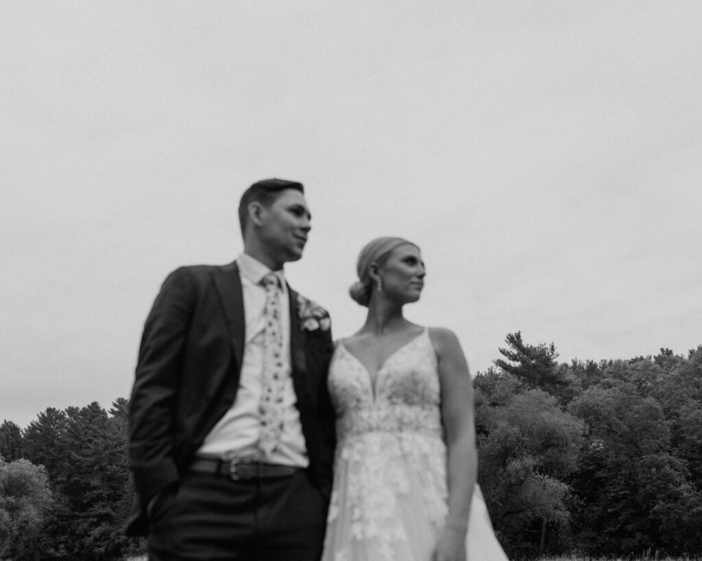 An out of focus black and white image of the bride and groom standing next to one another and looking off into the distance. 