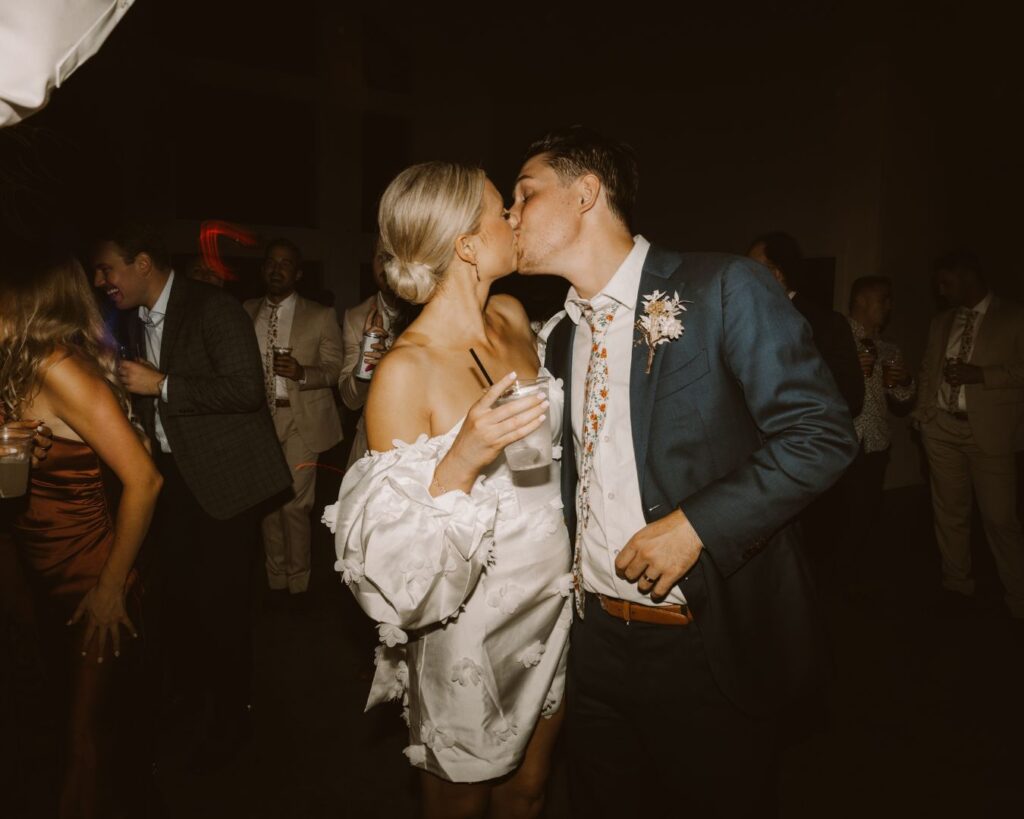 The bride and groom kissing surrounded by their guests on the dance floor 