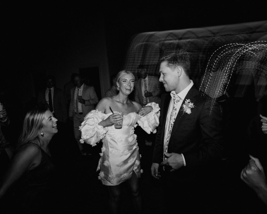 A black and white image of the bride and groom dancing surrounded by their guests on the dance floor. 