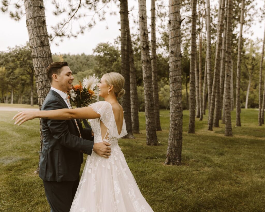 The bride and groom, surrounded by tall skinny pine trees, going in for a hug after seeing each other for the first time on their wedding day. 