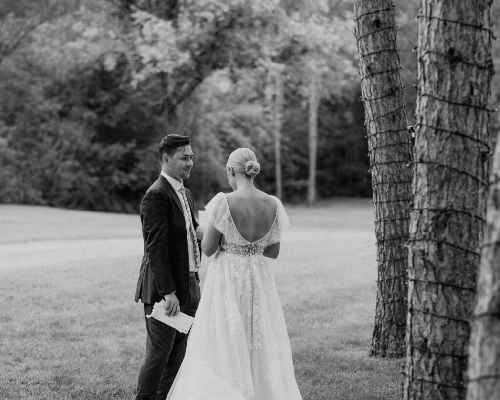 Black and white image of the bride and groom reading private vows to each other under towering pine trees. 