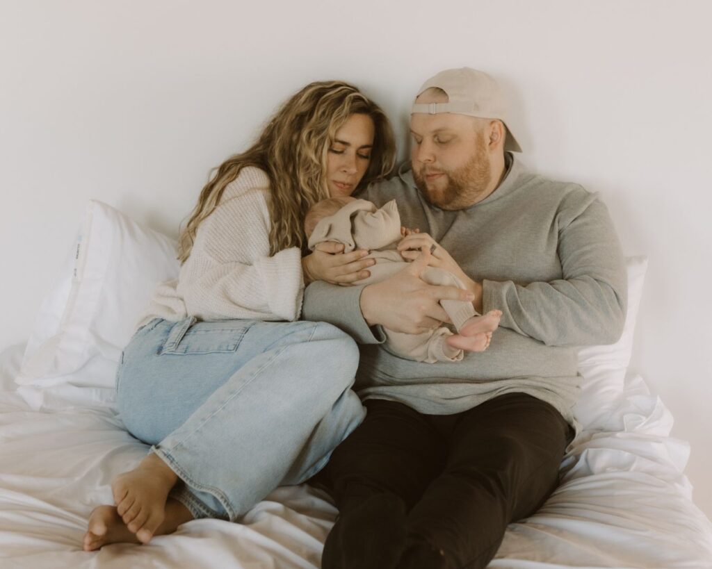 First-time mother and father cradle their newborn while snuggled up in bed.