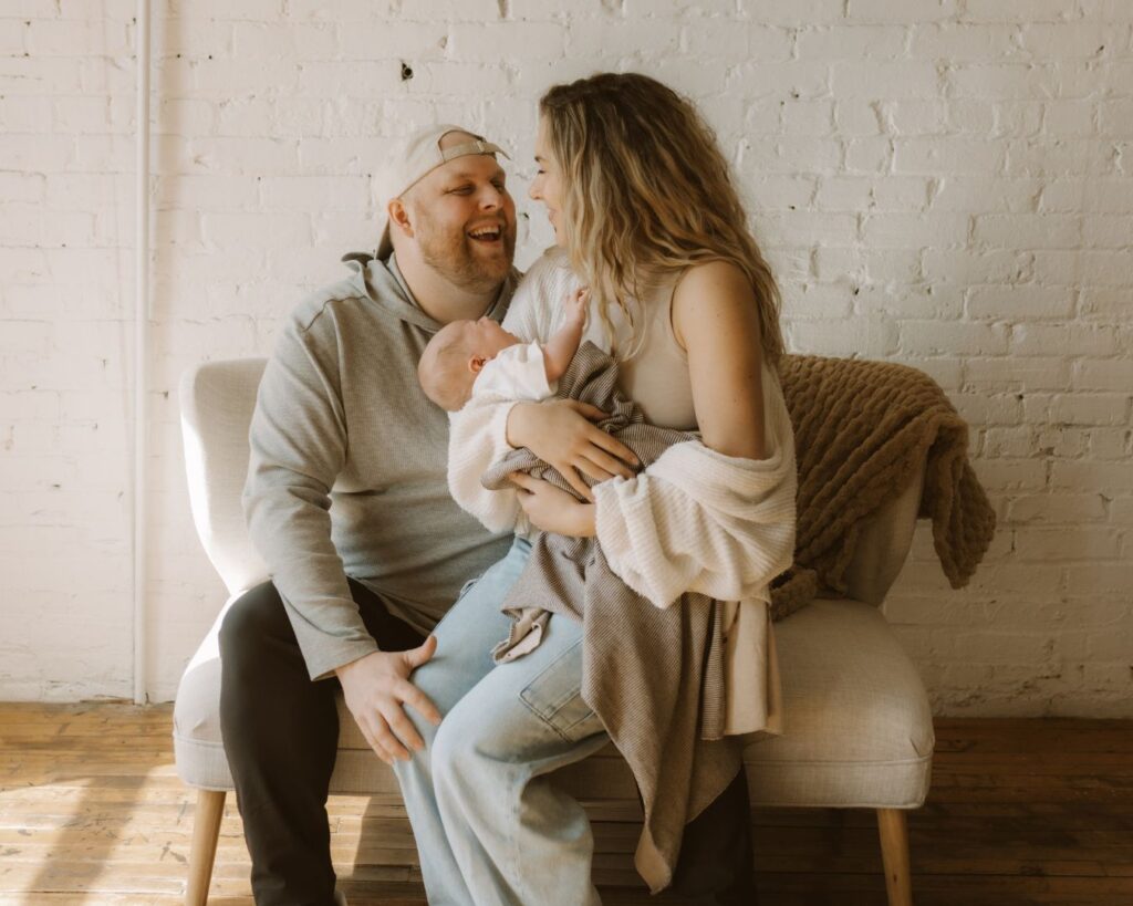 First-time mother and father smile at each other while snuggling their newborn on the couch