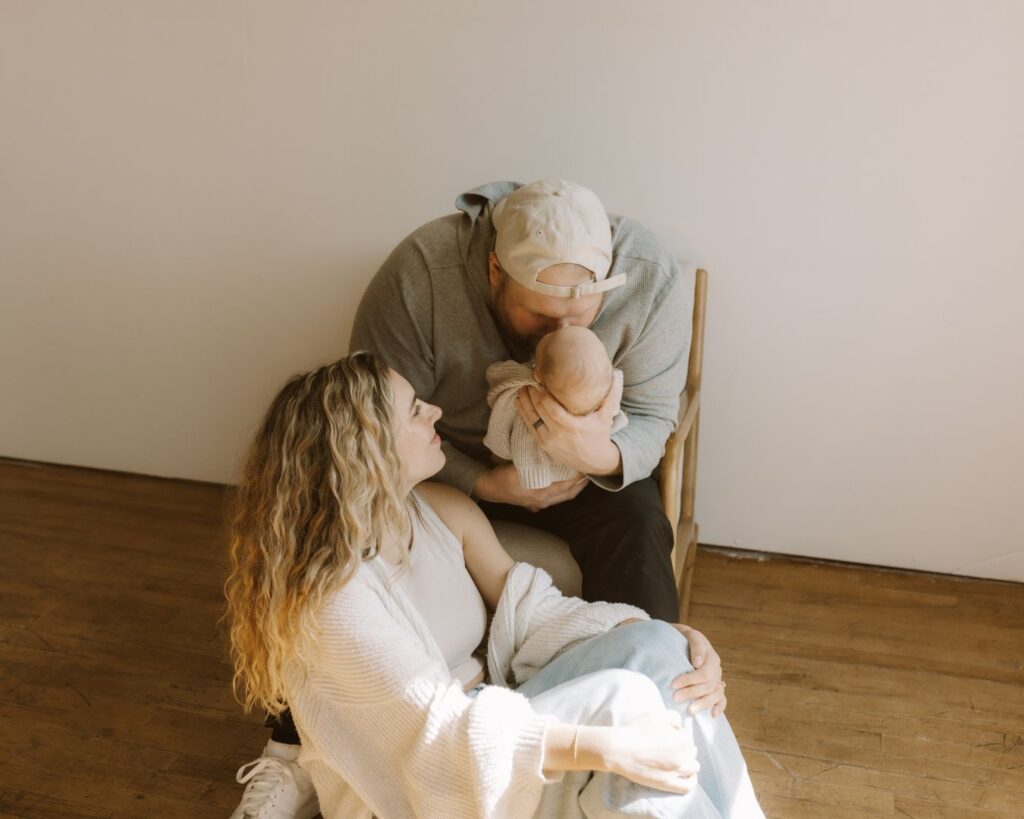 Mom sits on the floor and looks lovingly at her husband holding their baby boy during newborn photoshoot