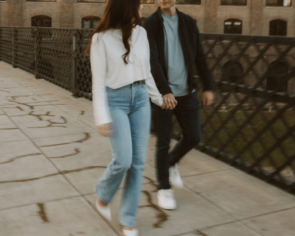 Slow shutter image of an engaged couple as they walk over a bridge in the city