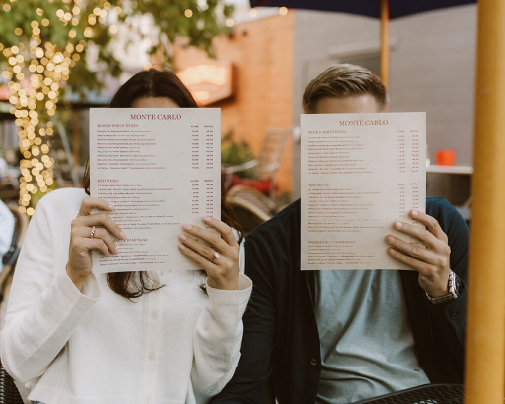 Engaged couple holding menus in front of their faces at their favorite neighborhood restaurant