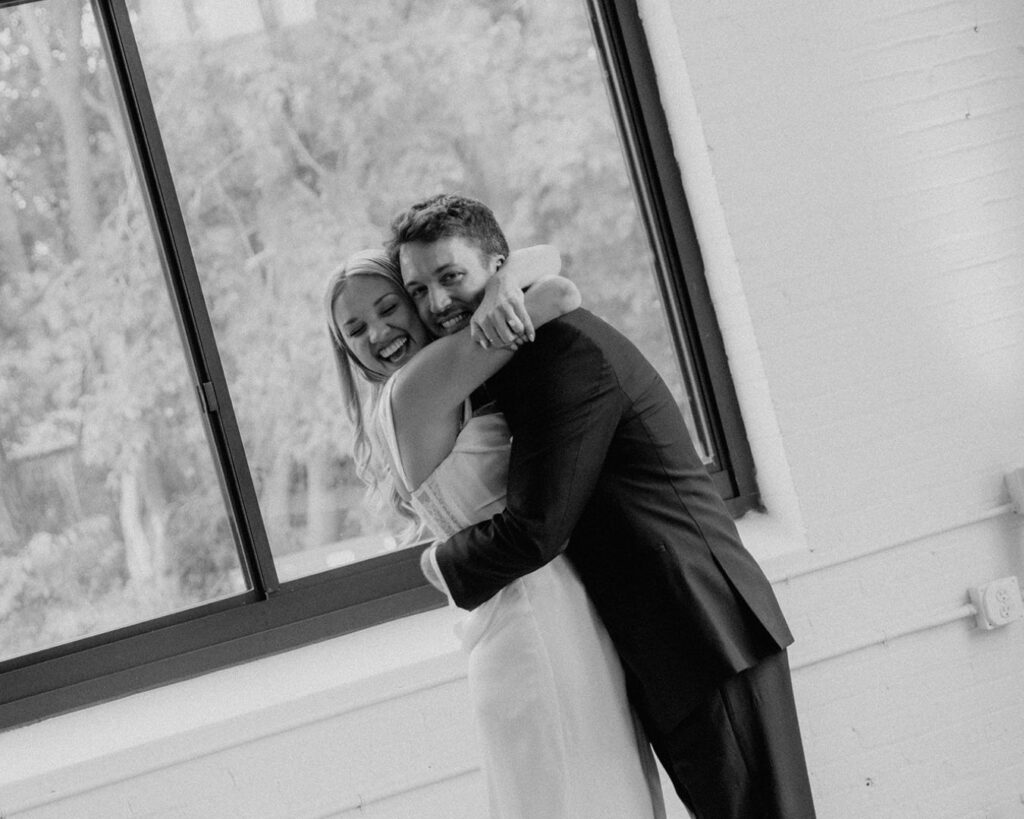 black and white image of the bride and groom hugging tightly and smiling ear to ear 