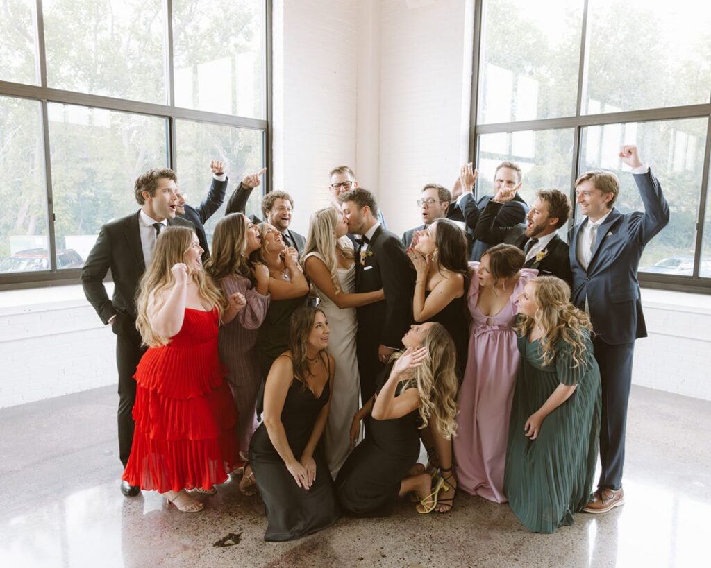 the bride and groom kissing while all their friends cheer and celebrate around them