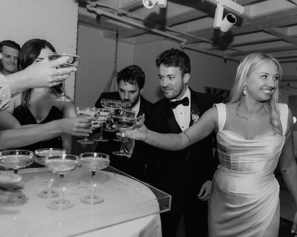 black and white image of the bride and groom doing a cheers with their closest friends and family 