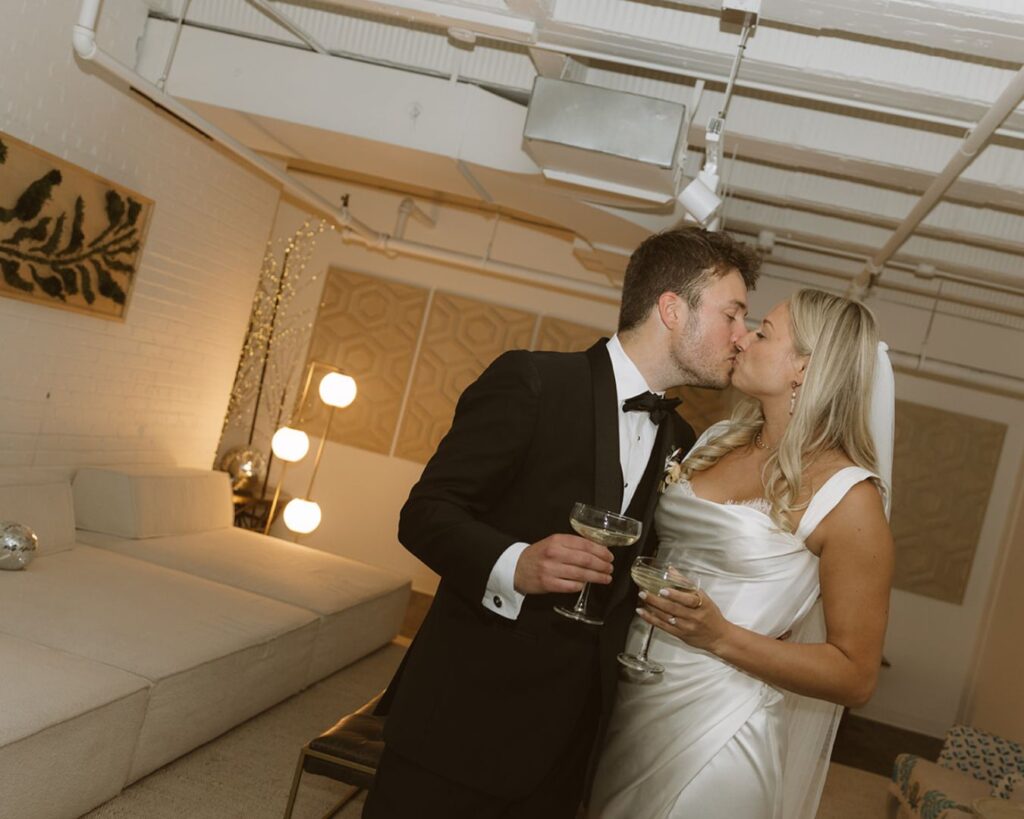 bride and groom kissing while holding their glasses of champagne