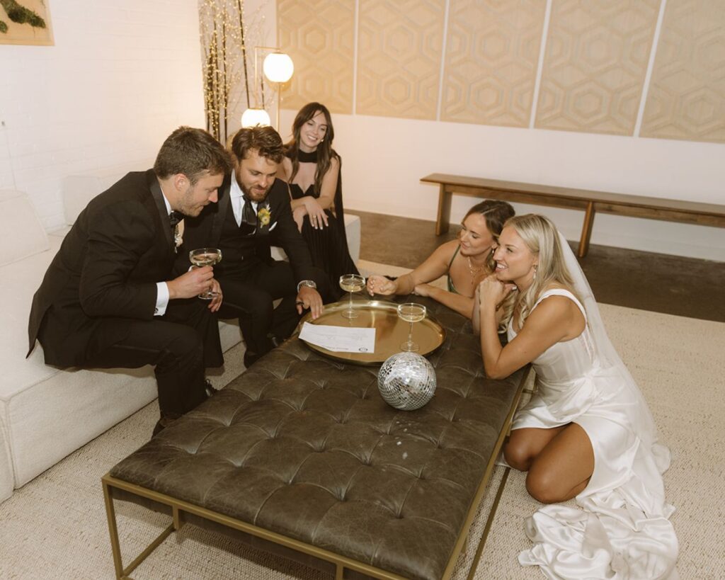 The bride, groom, made of honor, best man, and officiant gathered around a coffee table to sign the marriage license. The bride and maid of honor are sitting on the ground and the other three are on a couch. 