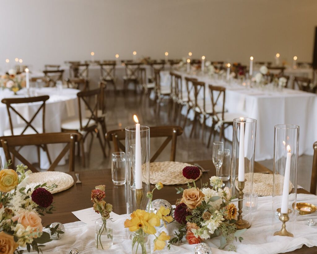 a up close photo of the head table set up at the reception  with candles, warm colored florals, and small disco balls before anyone has entered the room 