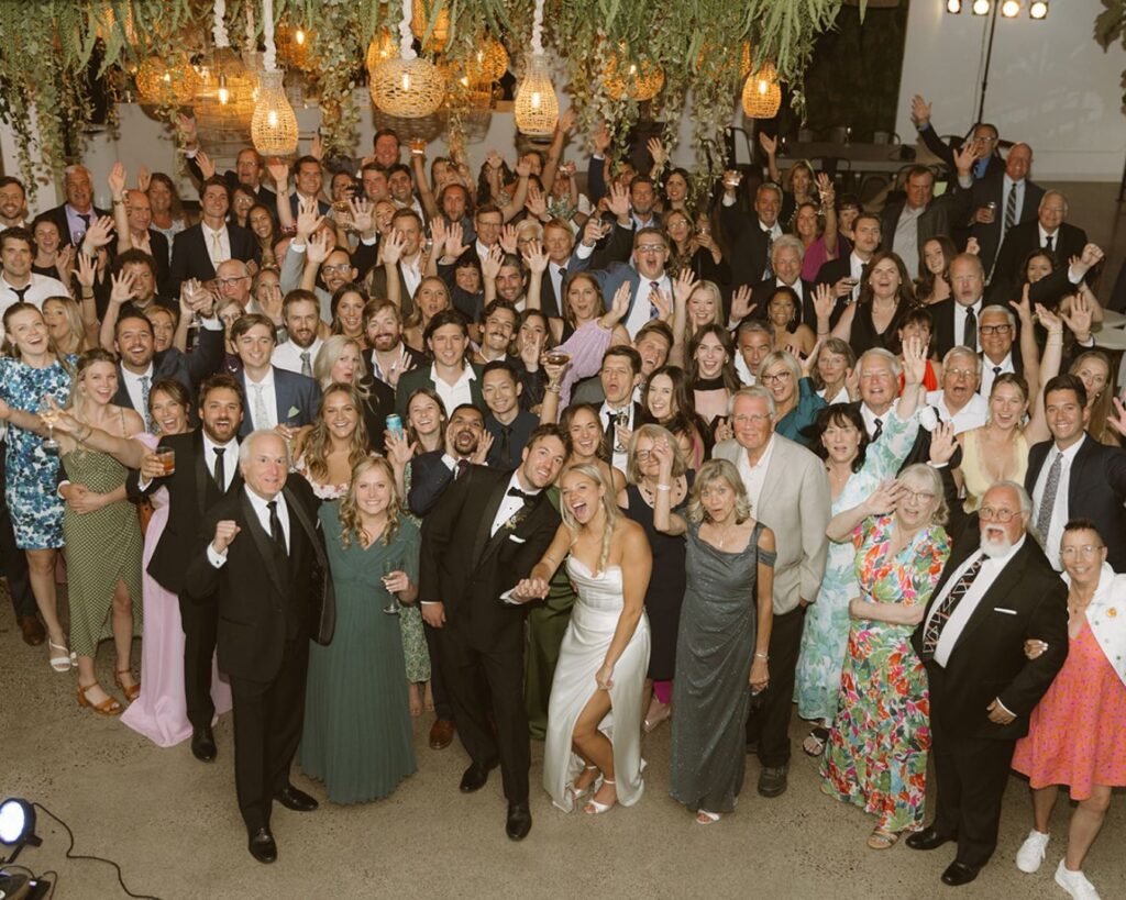 a giant group photo on the dance floor with the bride and groom front and center and all their guests cheering around and behind them