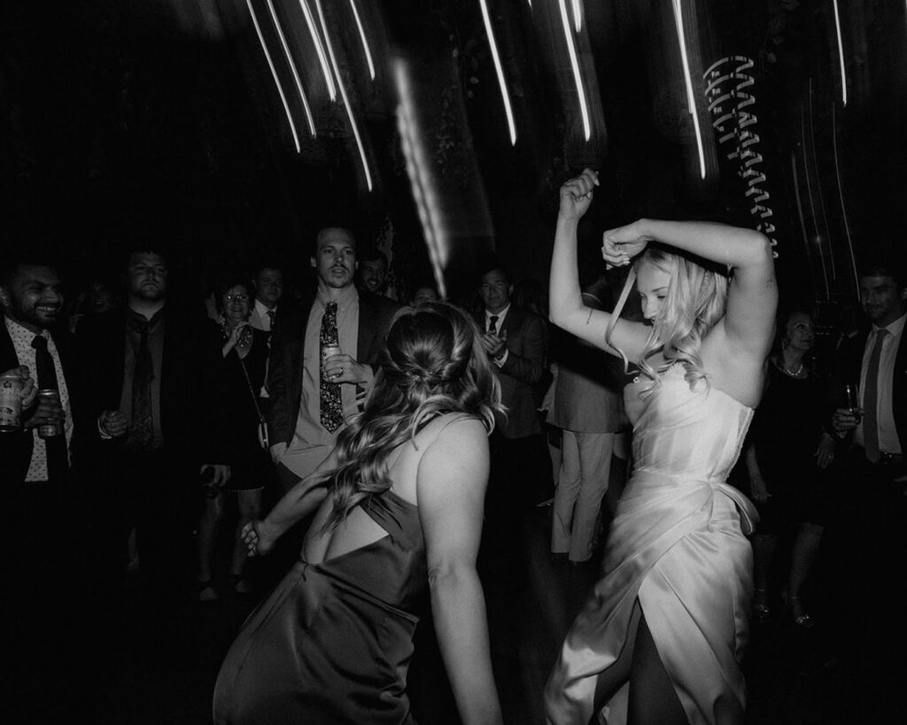 a black and white photo of the bride and her maid of honor dancing their hearts out 