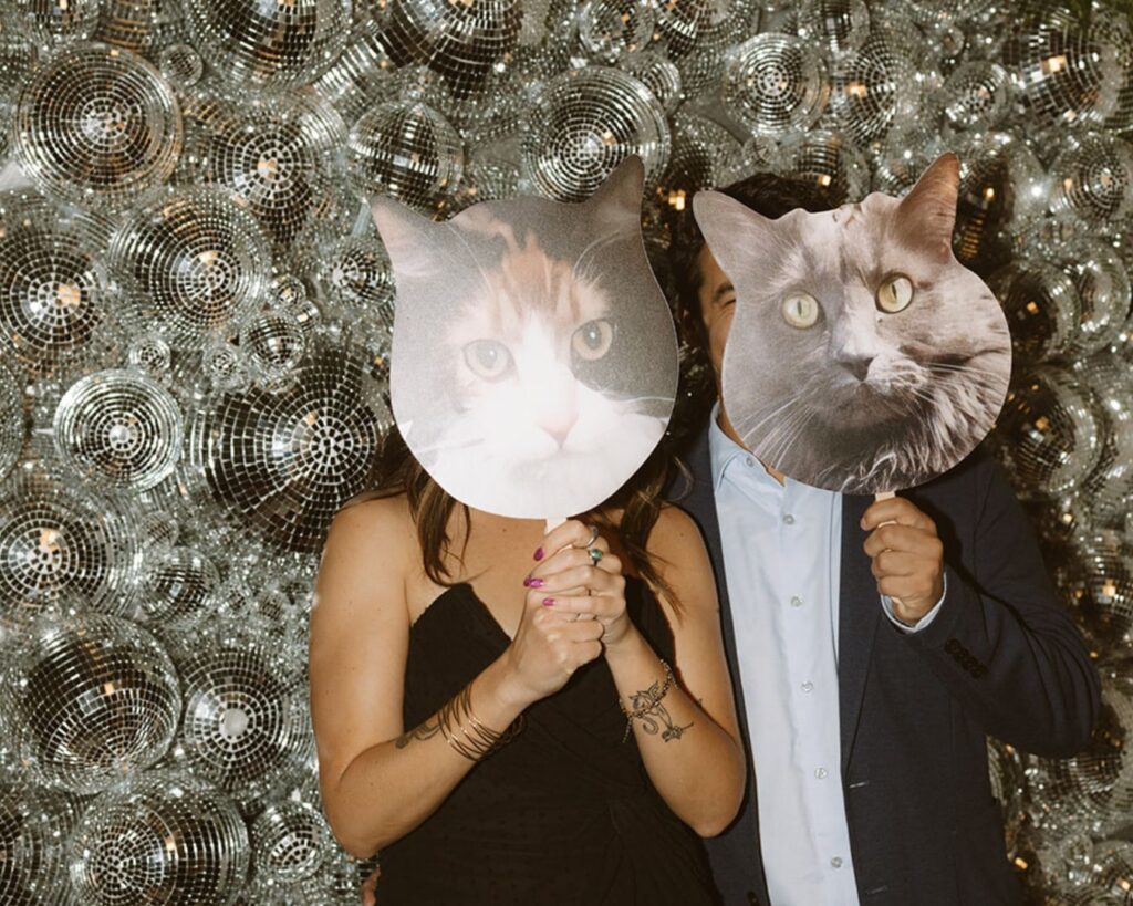 two guests holding up giant cutouts of the bride and groom's cat's heads at the photo booth