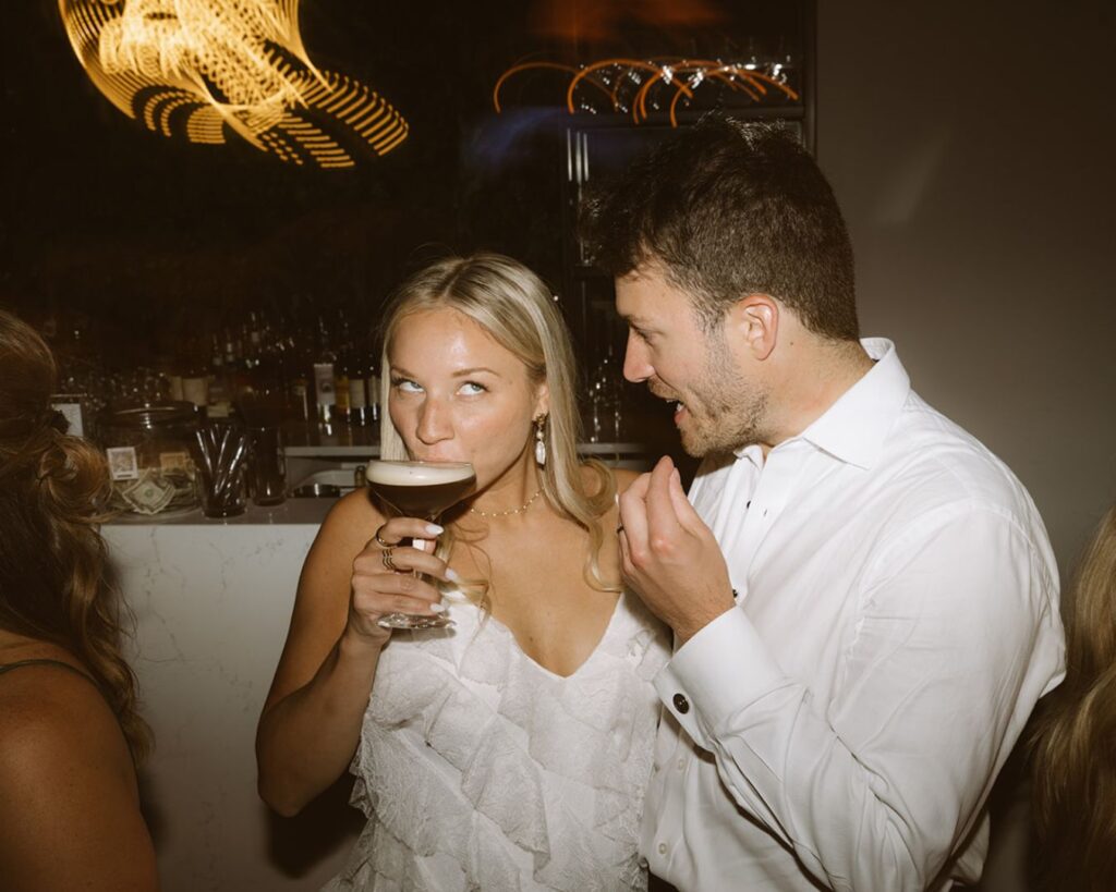 the bride making a silly face as she takes a sip of her espresso martini while the groom is saying something to her