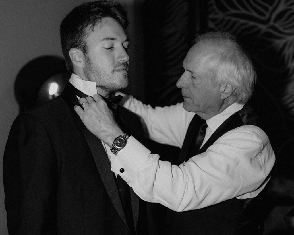 black and white image of the groom's father helping him put on his bowtie