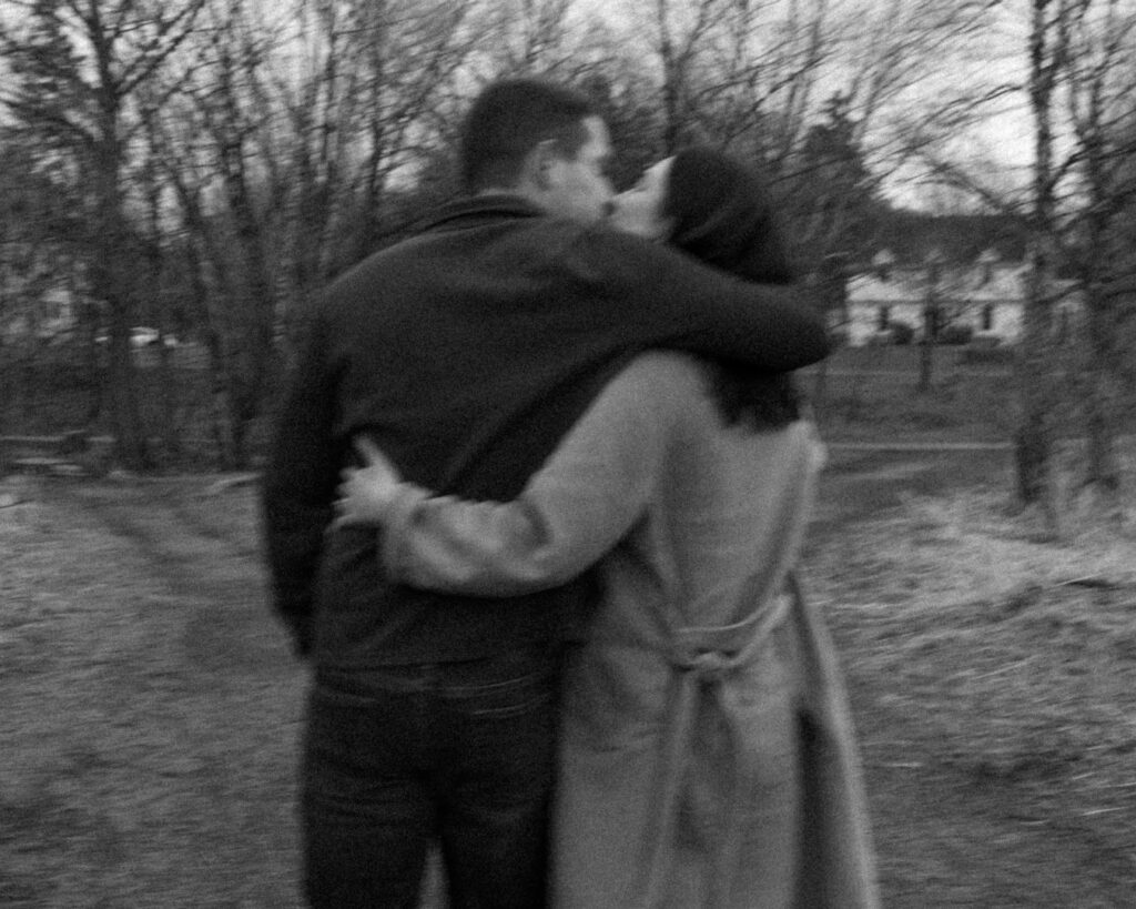 Black and white slow shutter image of a couple from behind as they walk arm in arm and sneak a kiss. 