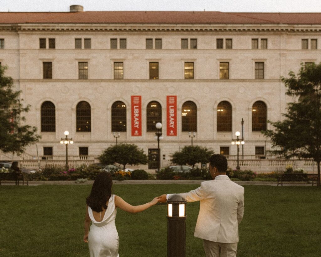 A couple holding hands and walking away towards the St. Paul Public library at dusk. 