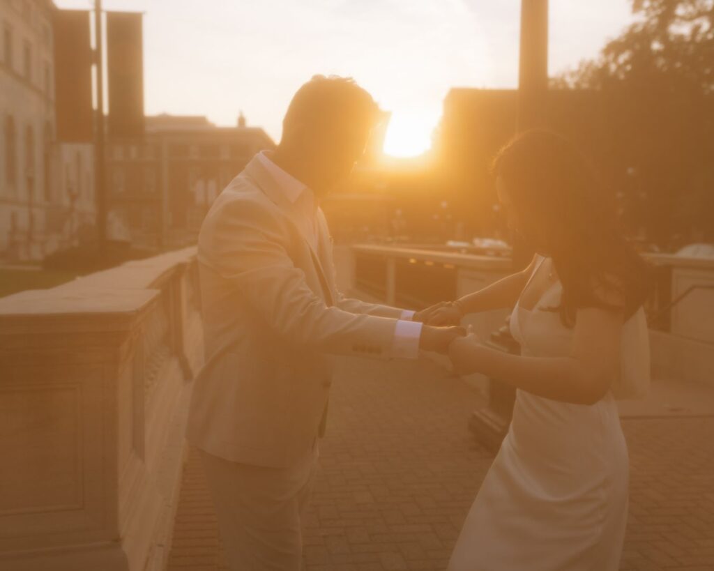 A couple holding both hands as they are covered in the golden light of a setting sun. 